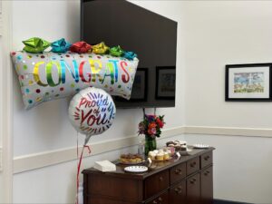 Two Mylar balloons that say "Congrats" and "Proud of You" float next to a sideboard with plates of cupcakes resting on top