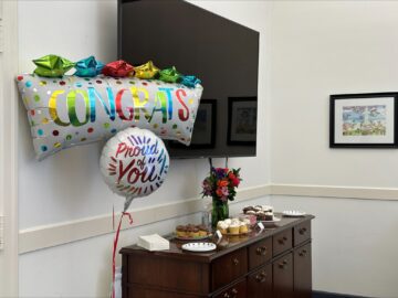 Two Mylar balloons that say "Congrats" and "Proud of You" float next to a sideboard with plates of cupcakes resting on top