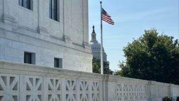 The U.S. Capitol dome emerges from behind the U.S. Supreme Court building and an American flag blows in the breeze